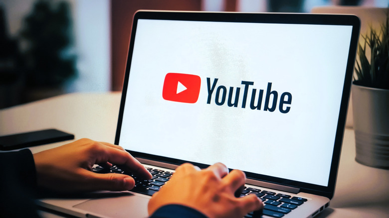 YouTube logo on a laptop screen with hands typing on the keyboard