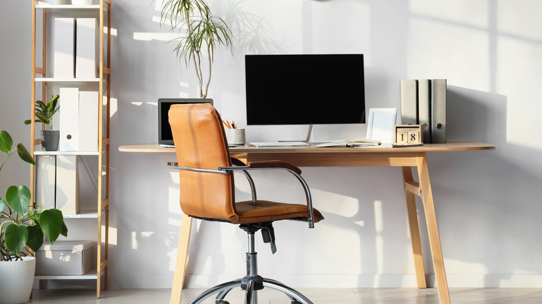 A brightly lit modern home office workspace with a computer monitor, laptop, and a chair