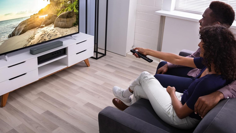 A couple watches a TV with the Westinghouse 2.0-channel soundbar positioned beneath it