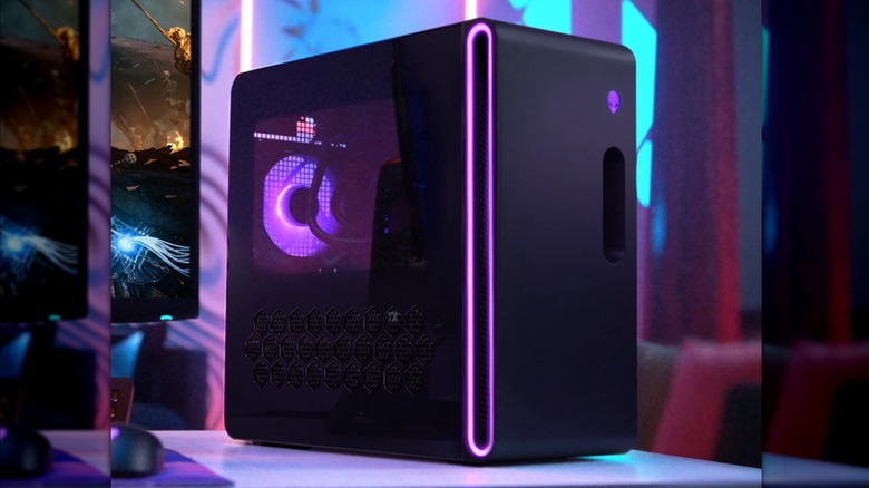 A black Dell Alienware Aurora ACT1250 Gaming PC displaying purple illuminated trim, the device itself is next to a gaming monitor
