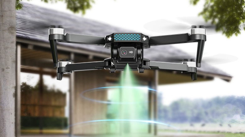 A Deerc D20S drone hovers outside with a the corner of a house standing behind it