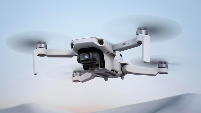 A white Dji Mini is hovering in the air using its four rotating propellers