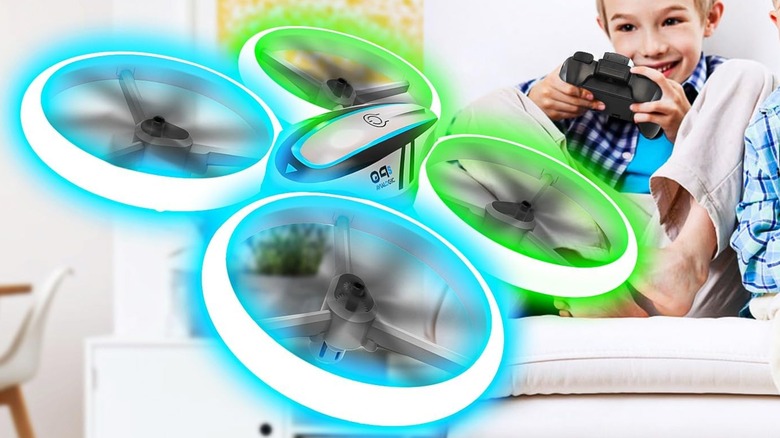 A Hasakee Q9 drone hovers in a living room as a young individual sitting on a couch looks to be controlling it with the two-handed controller