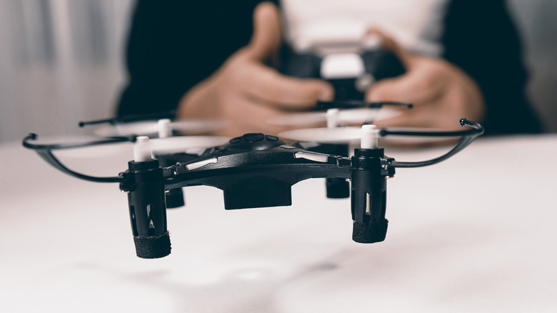 A closeup of a small black drone as it hovers close to a white table