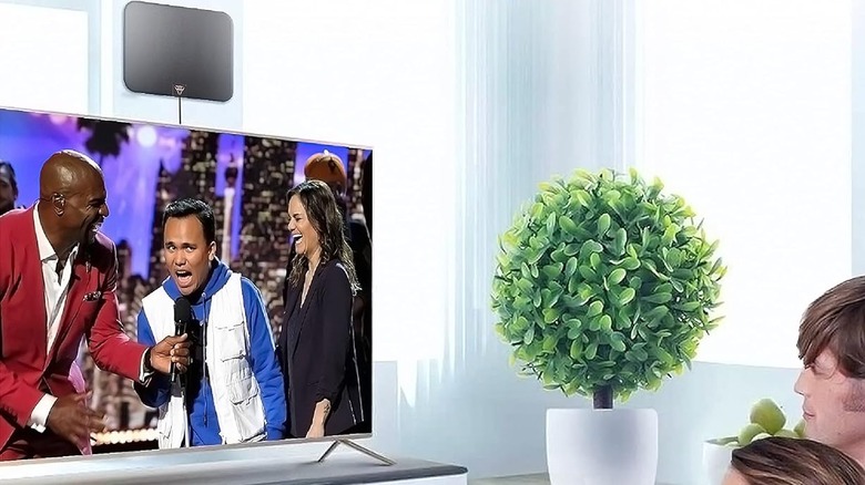 The Gesobyte Indoor Antenna mounted above a tabletop TV, as a couple sits on a couch watching a broadcast.