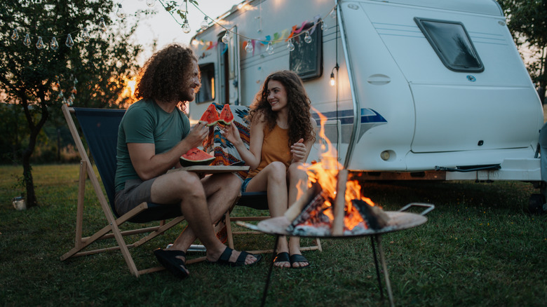 Two people enjoying a sunset and slices of watermelon in front of a camper.