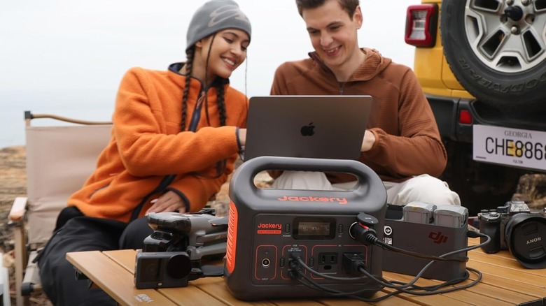 Two people using the Jackery 300 Portable Power Station outdoors to power an Apple laptop.