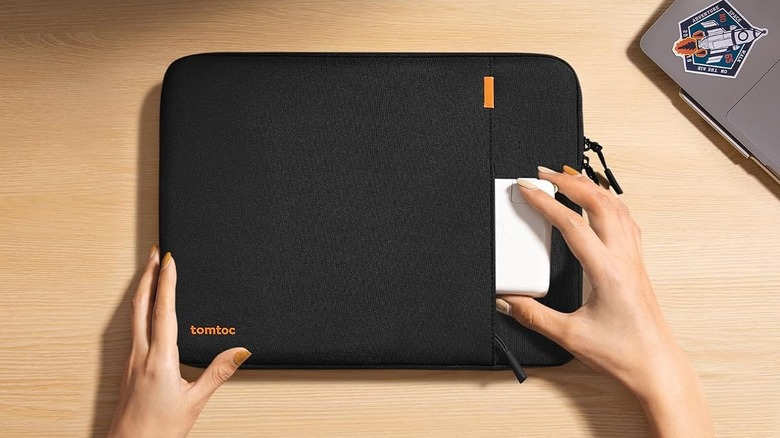 A person putting a laptop charger in the pocket of a tomtoc 14-inch Protective Laptop Sleeve on a desk.