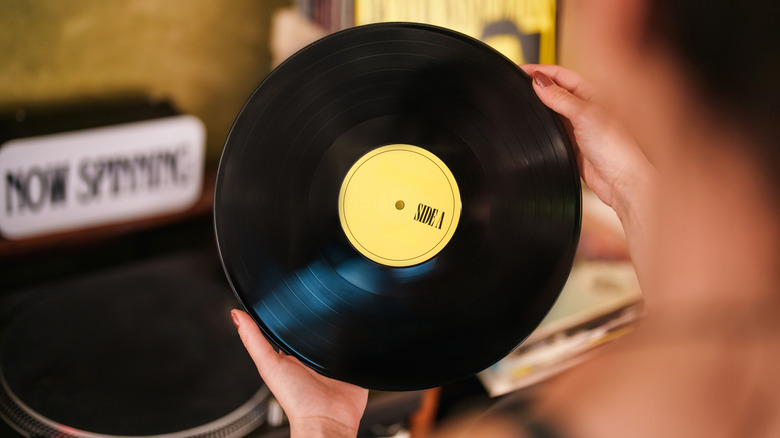 An individual holding a vinyl record in their hands, the vinyl has a yellow sticker in the center that says "Side A"
