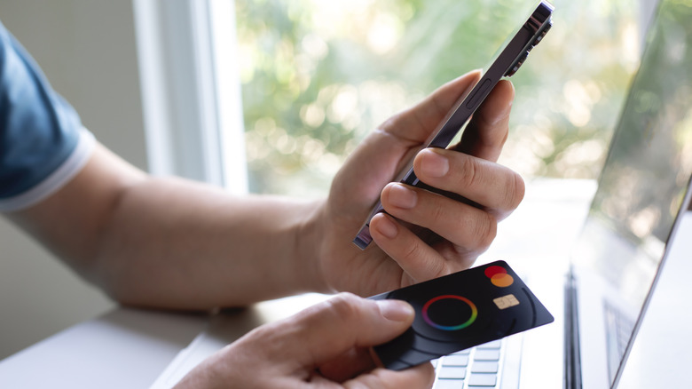 A person holding an iPhone in one hand and a physical credit card in the other.
