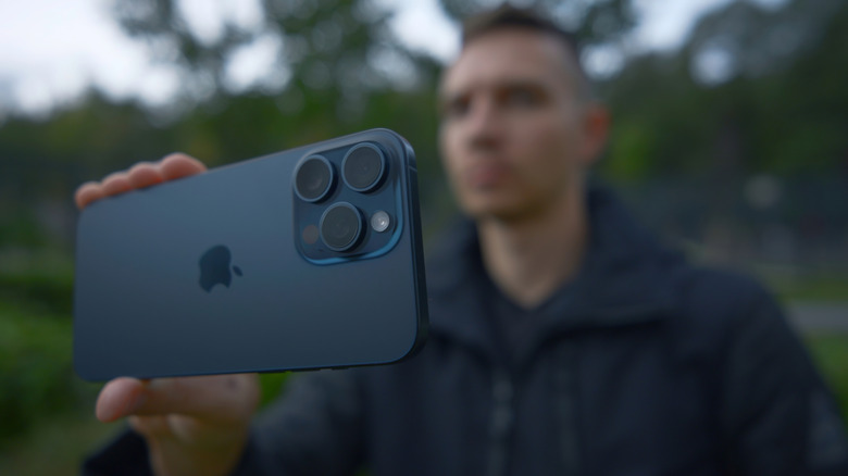 Man holding an Apple iPhone 15 Pro smartphone in outdoor setting