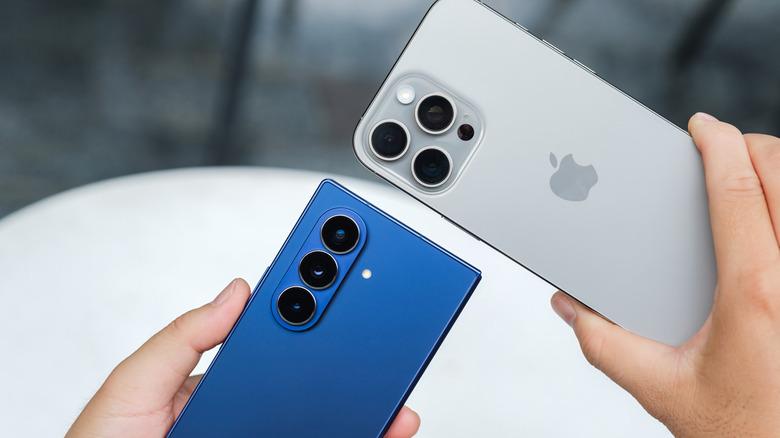 Hands holding an iPhone and Samsung smartphone in each hand