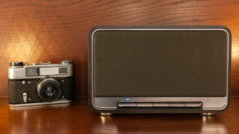A retro speaker placed next to a film camera on a shelf.