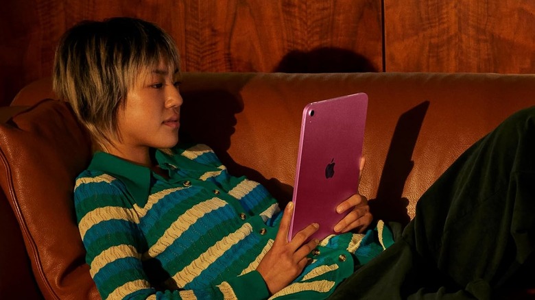 An individual in a striped shirt sitting on a brown leather couch holds a pink Apple iPad between their hands