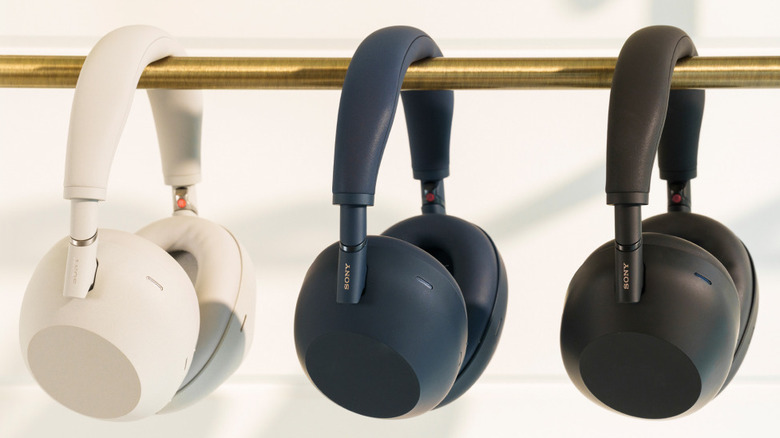 Sony WH-1000XM6 wireless headphones displayed hanging from a metal rail, shown in white, blue, and black color options