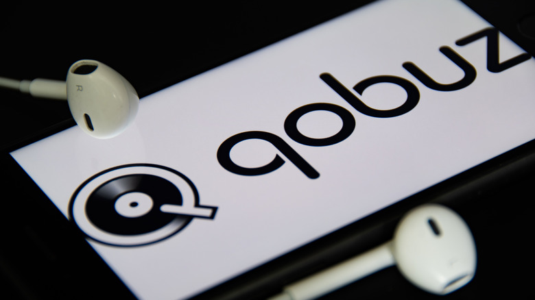Qobuz logo displayed on a smartphone screen with wired earbuds beside it.