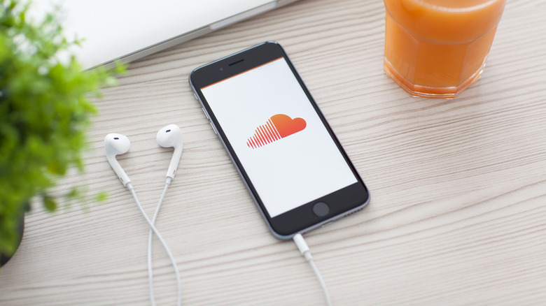 Smartphone displaying the SoundCloud logo beside wired earbuds on a table.