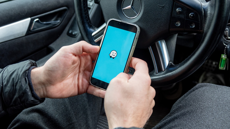 An individual holding a phone showing the Waze logo inside a car