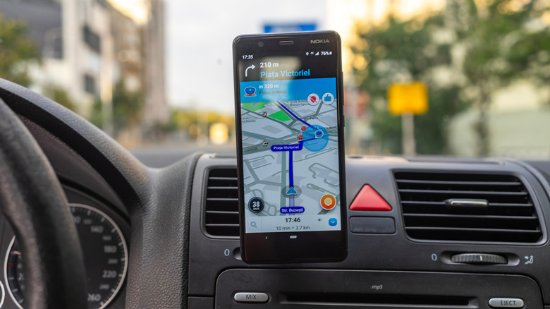A black smartphone hangs from a black dashboard showing the Waze app