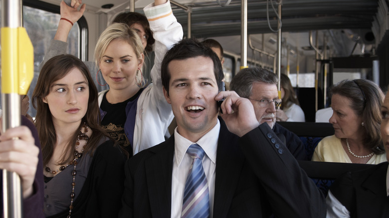 A man in a suit taking a call in a bus surrounded by other people