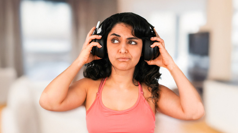A woman with headphones on making a confused expression