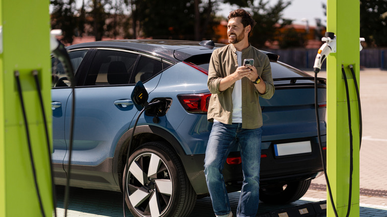 Person using a phone standing next to a charging EV