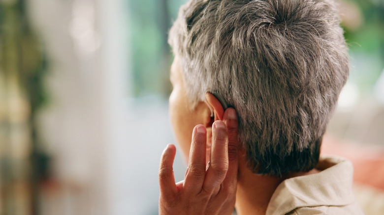 An old person putting their hand on the back of their ear, trying to listen to something