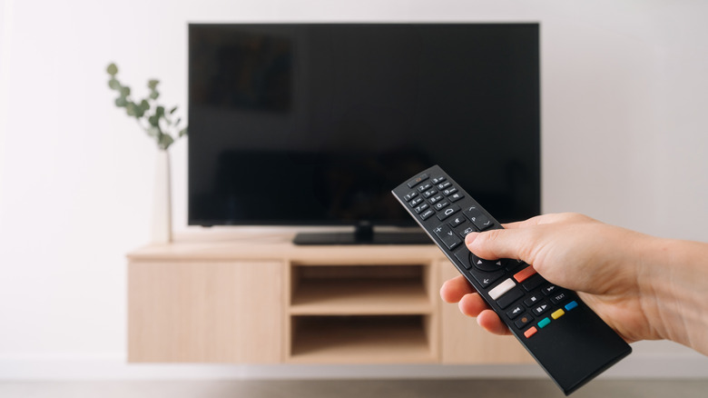 A person aiming a remote at their TV, which is showing a black screen