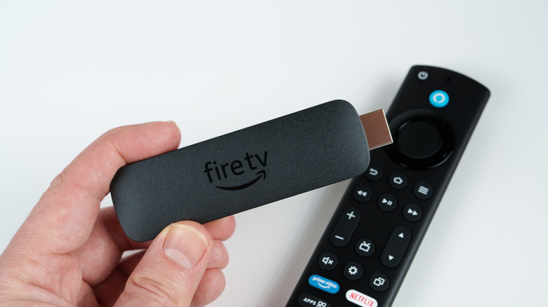Close up of hand holding the Amazon Fire TV Stick, a USB stick that has a firetv logo on it