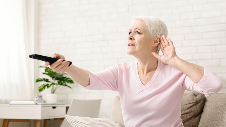 Woman gesturing "can't hear anything" while holding TV remote