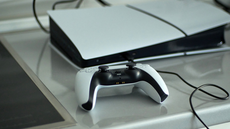 DualSense controller in front of the PlayStation 5 console on a table surface with a wire