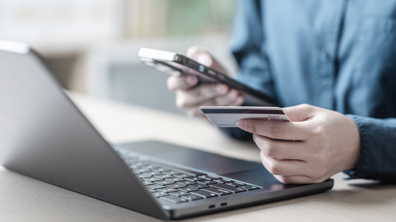 A man holding a cell phone and a credit card while referencing something on a laptop.