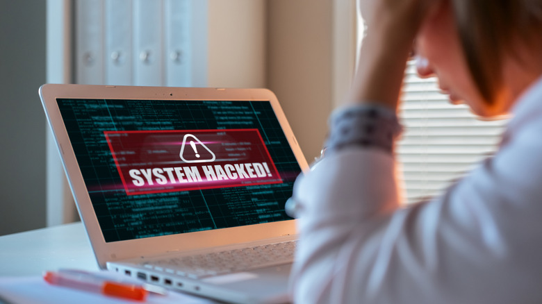 women looking at a laptop screen that says System Hacked