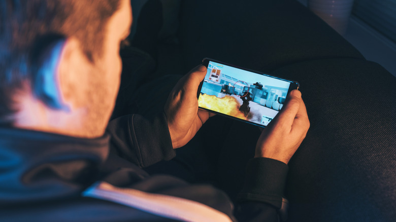 A person sitting down playing an action-shooter game on their phone