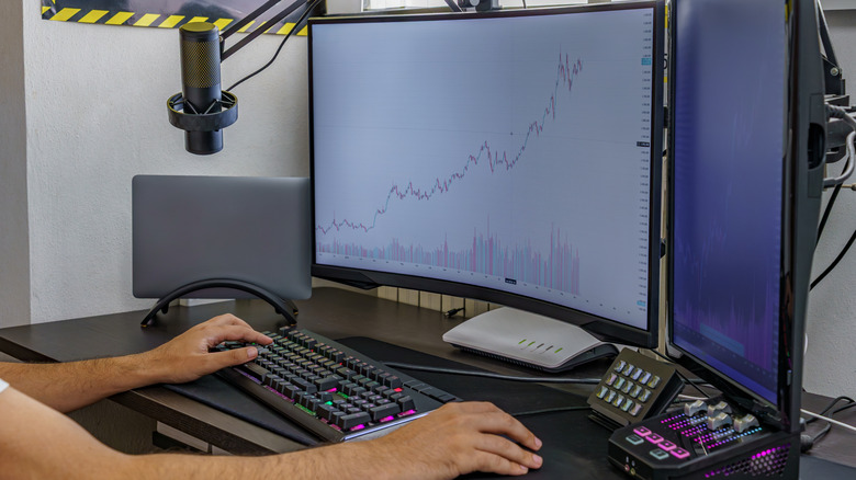 A person sitting in front of dual monitor setup displaying financial charts