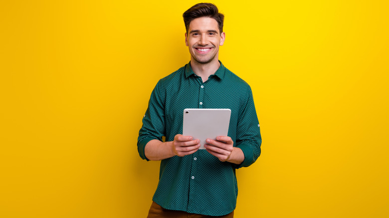 A happy person holding an iPad standing in front of a yellow background