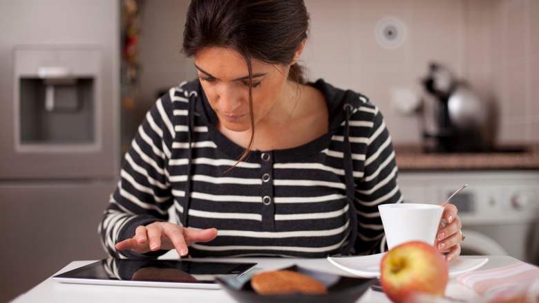 Woman sitting in a kitchen using a computer tablet
