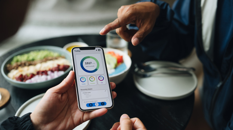 A close-up shot of two people viewing a calorie counting app that displays daily calories and a macro-nutrient breakdown.