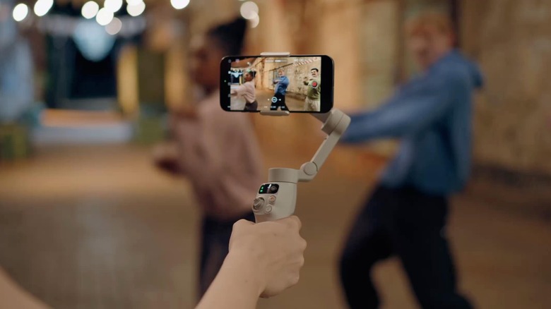 A person using the DJI Osmo Mobile 8 gimbal, with their phone attached to it, to record people dancing