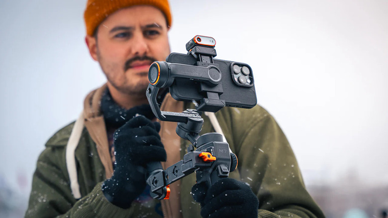 A person using the Hohem iSteady M7 gimbal in winter, with a phone attached to it