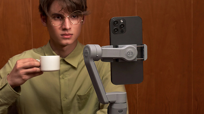 A person holding a coffee cup while looking at their phone, which is attached to the Zhiyun Smooth Q4