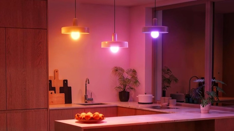 A kitchen island lit up by three colored ceiling lights — one orange, one pink, and one purple.