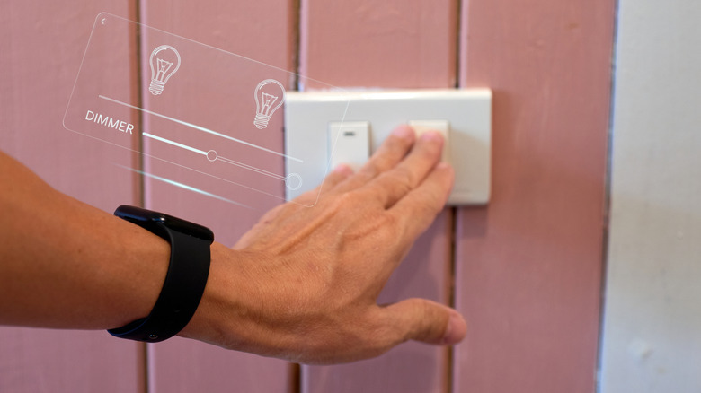 A hand touching a wall-mounted smart dimmer switch beside a graphic overlay of a light bulb dimmer slider.