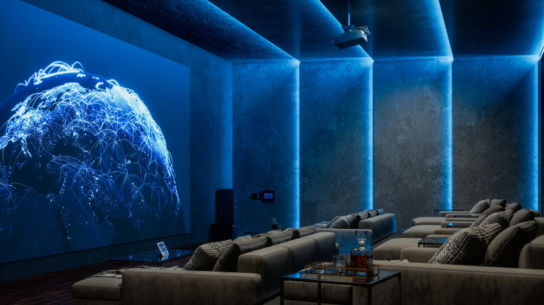 A luxury home theater featuring multiple gray sofas, vertical neon blue lights, and a projected graphic of blue flight paths on a blue globe.