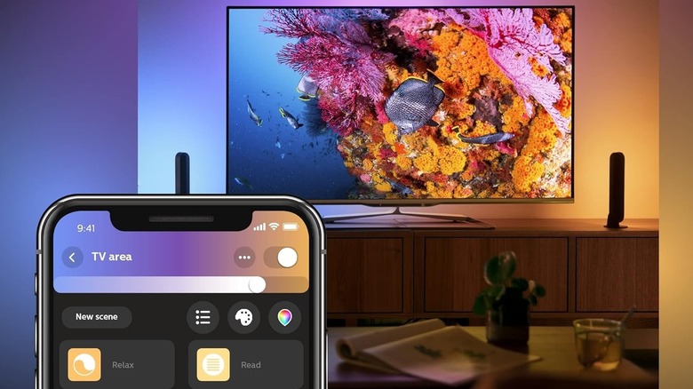 Hue Play light bars, one set to blue and one set to orange, on either side of a TV with the Hue app in the foreground.