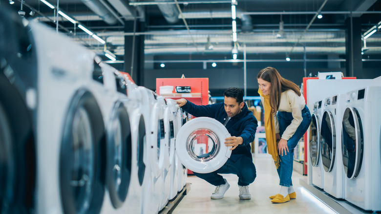A man and woman looking at washing machines on sale at an appliance store.