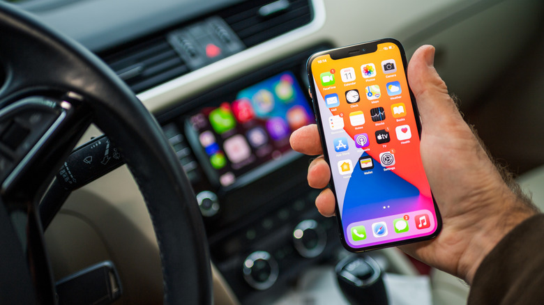 Male driver holding new iPhone 12 Pro smartphone with CarPlay
