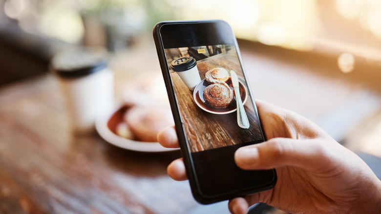 A phone, with someone taking a photo of two swirls and a coffee.