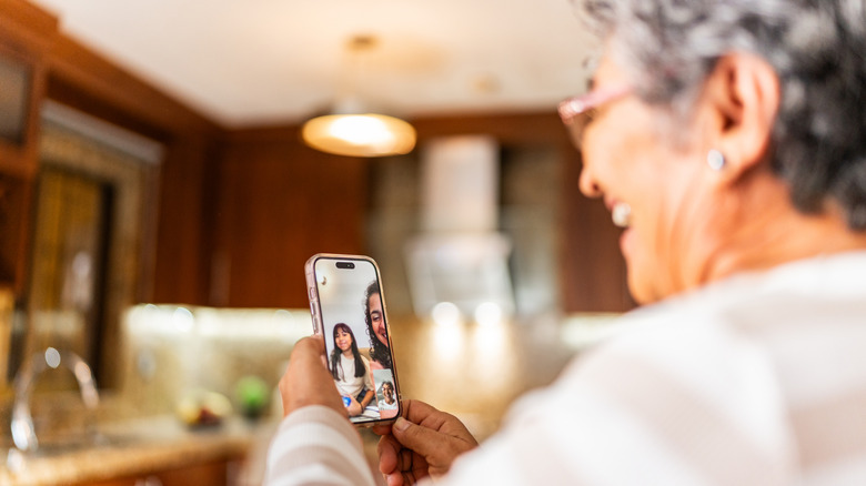 A senior woman holding a smartphone and having a video calling a woman and child