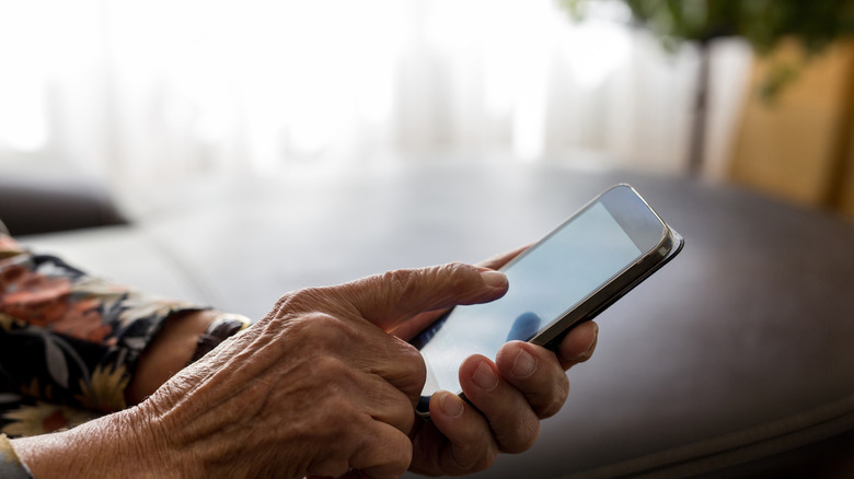 The hand of an older person touches a smartphone screen.